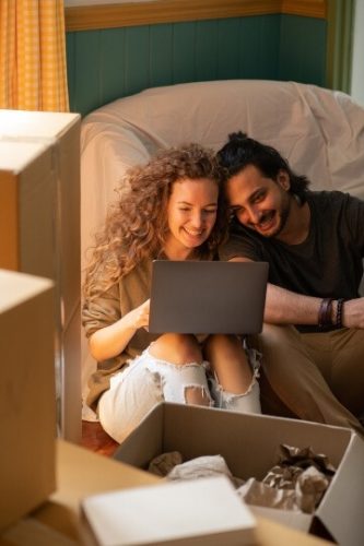Man and woman looking at a laptop, surrounded by packing boxes.