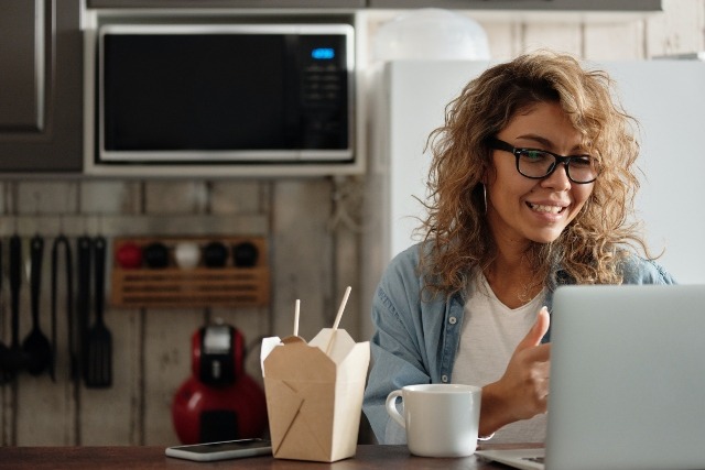 Woman eating Chinese takeout and looking at new homes on a laptop